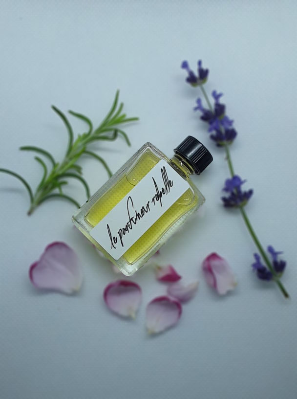 A clear bottle of natural perfume, with Le Parfumeur Rebelle Label and some wild flowers 